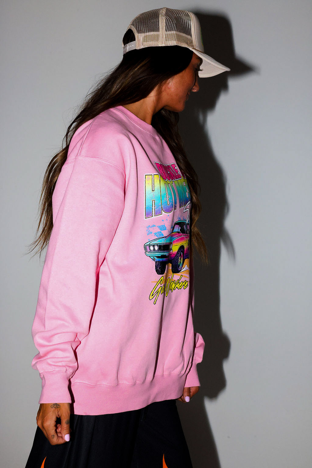 Model wearing a pink crewneck with a colorful graphic of a car and text on a plain background, side view