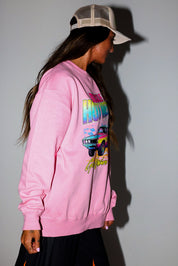 Model wearing a pink crewneck with a colorful graphic of a car and text on a plain background, side view
