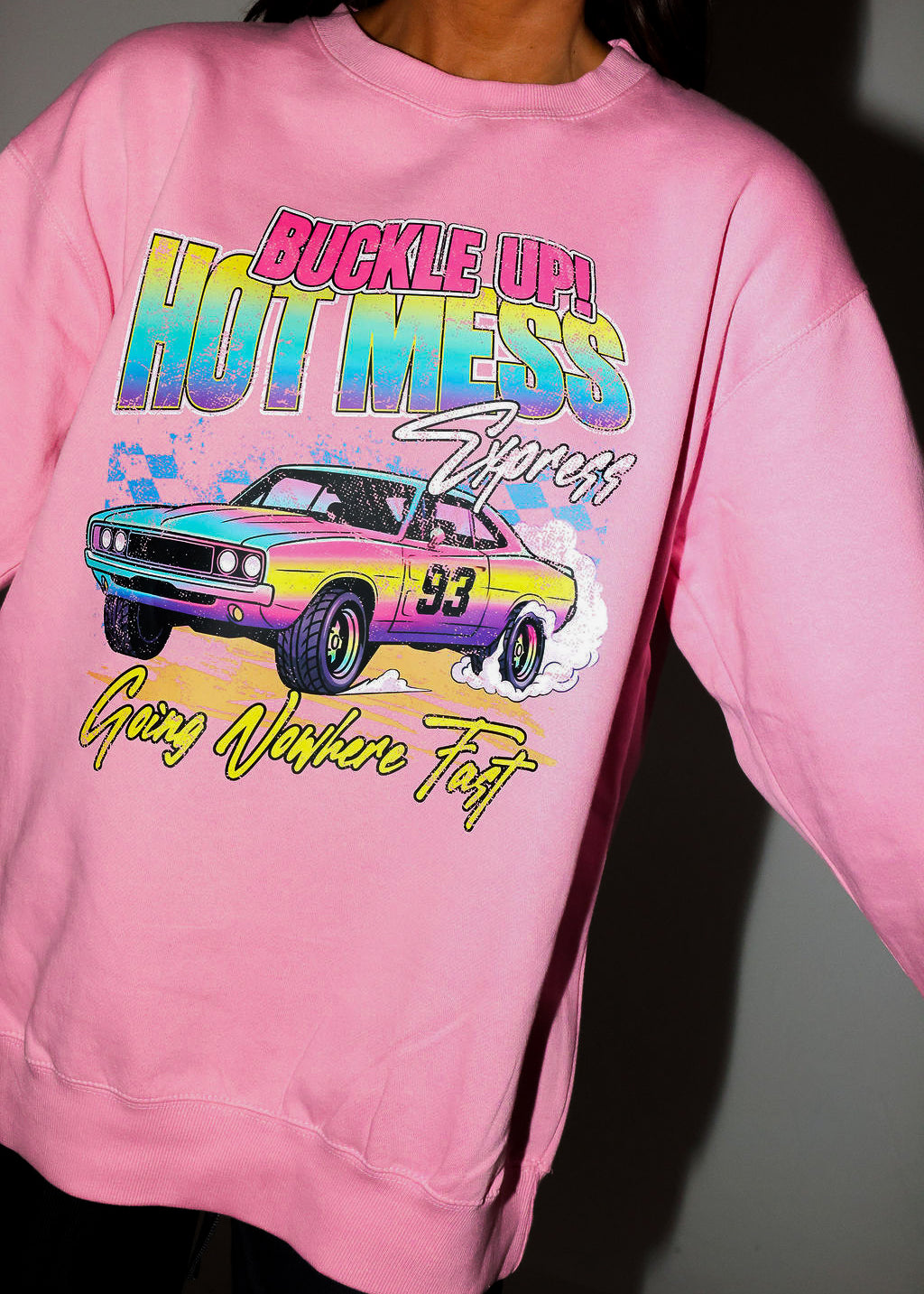 Model wearing a pink crewneck with a colorful graphic of a car and text on a plain background, frontal view