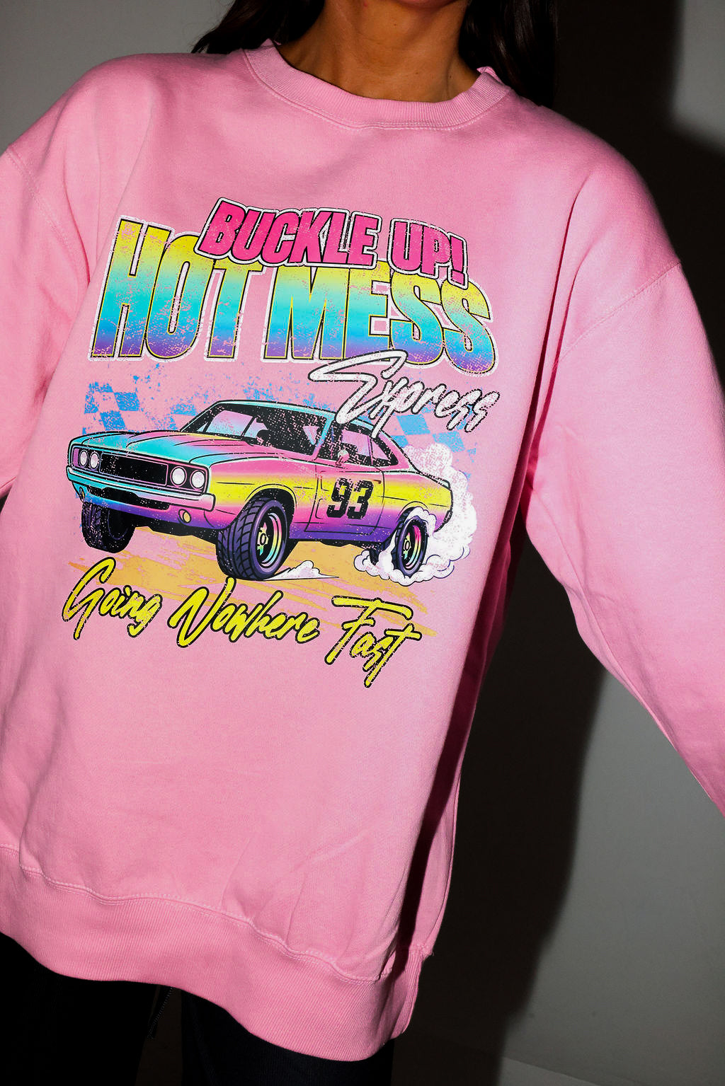 Model wearing a pink crewneck with a colorful graphic of a car and text on a plain background, frontal view