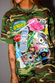 Model wearing camouflage t-shirt with colorful graphic designs and text on a plain background, close up frontal view