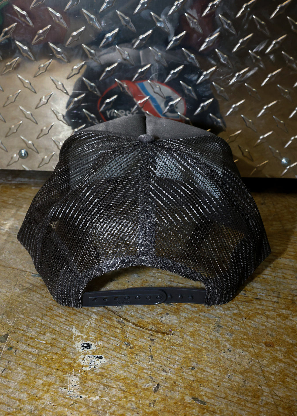Grey mesh trucker on a textured surface with a metallic background, back view