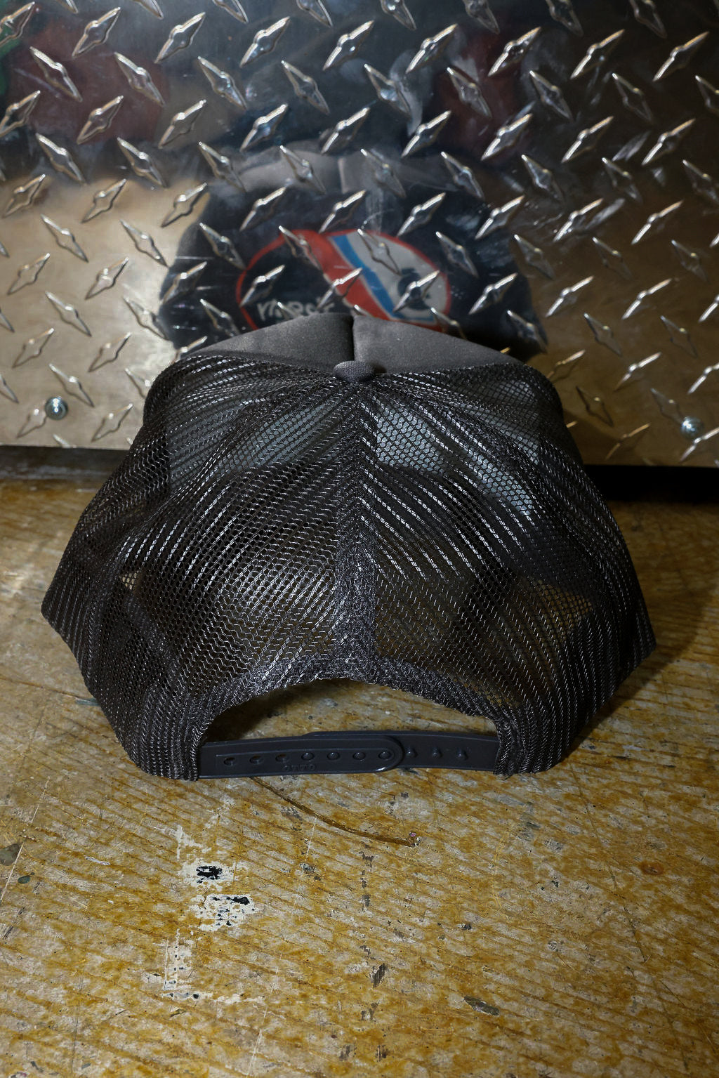 Grey mesh trucker on a textured surface with a metallic background, back view