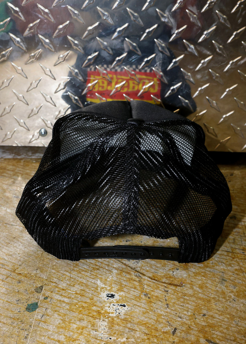 Black mesh trucker on a textured metal and wooden surface, back view