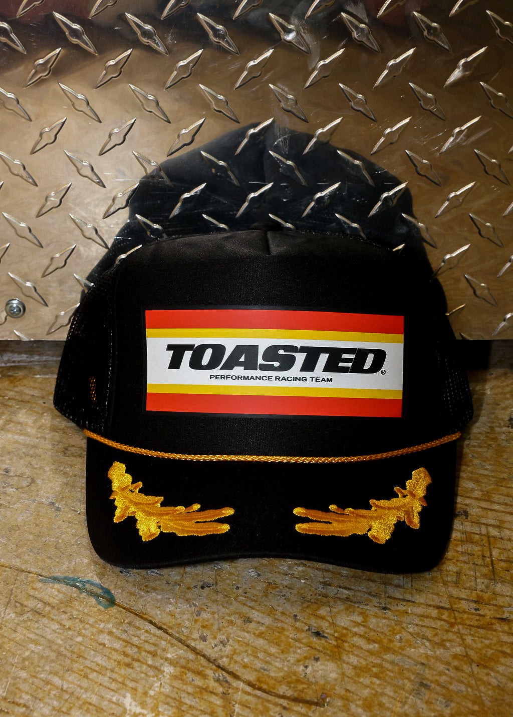 Black trucker with TOASTED logo and gold design, on a metallic background, frontal view
