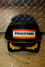 Black trucker with TOASTED logo and gold design, on a metallic background, frontal view