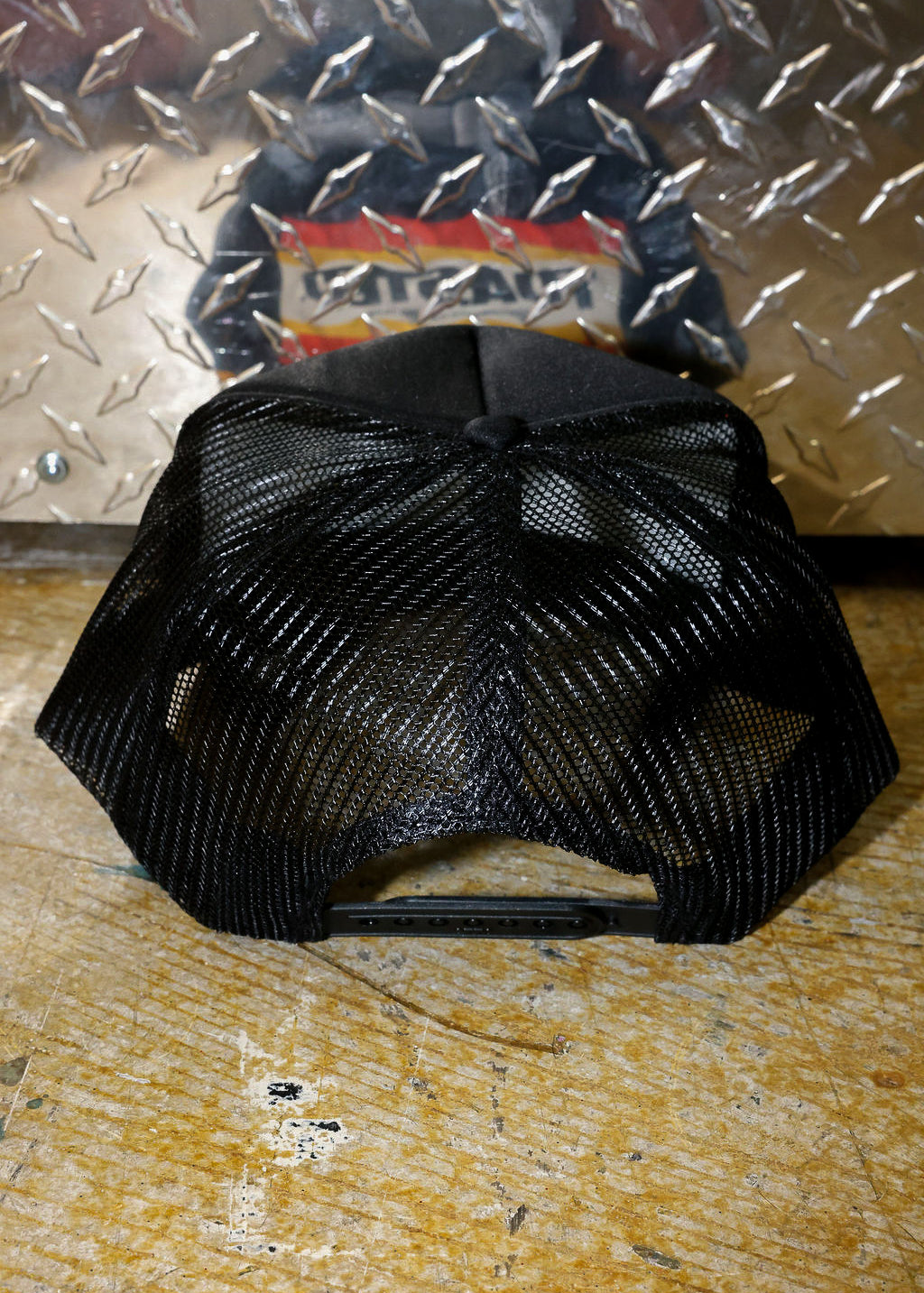 Black mesh trucker on a textured surface with a metallic background, back view