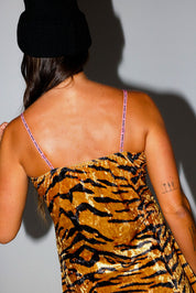 Woman wearing a tiger-striped dress with thin straps on a plain background, close up back view
