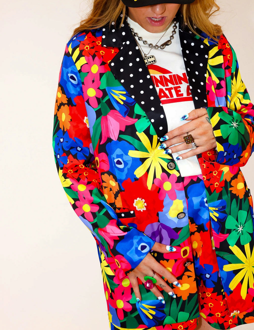 Model wearing a colorful floral jacket with polka dot collar, and matching shorts, a plain background, frontal view