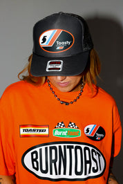 Model wearing a black trucker hat and orange shirt with 'Burntoast' branding, close up frontal view