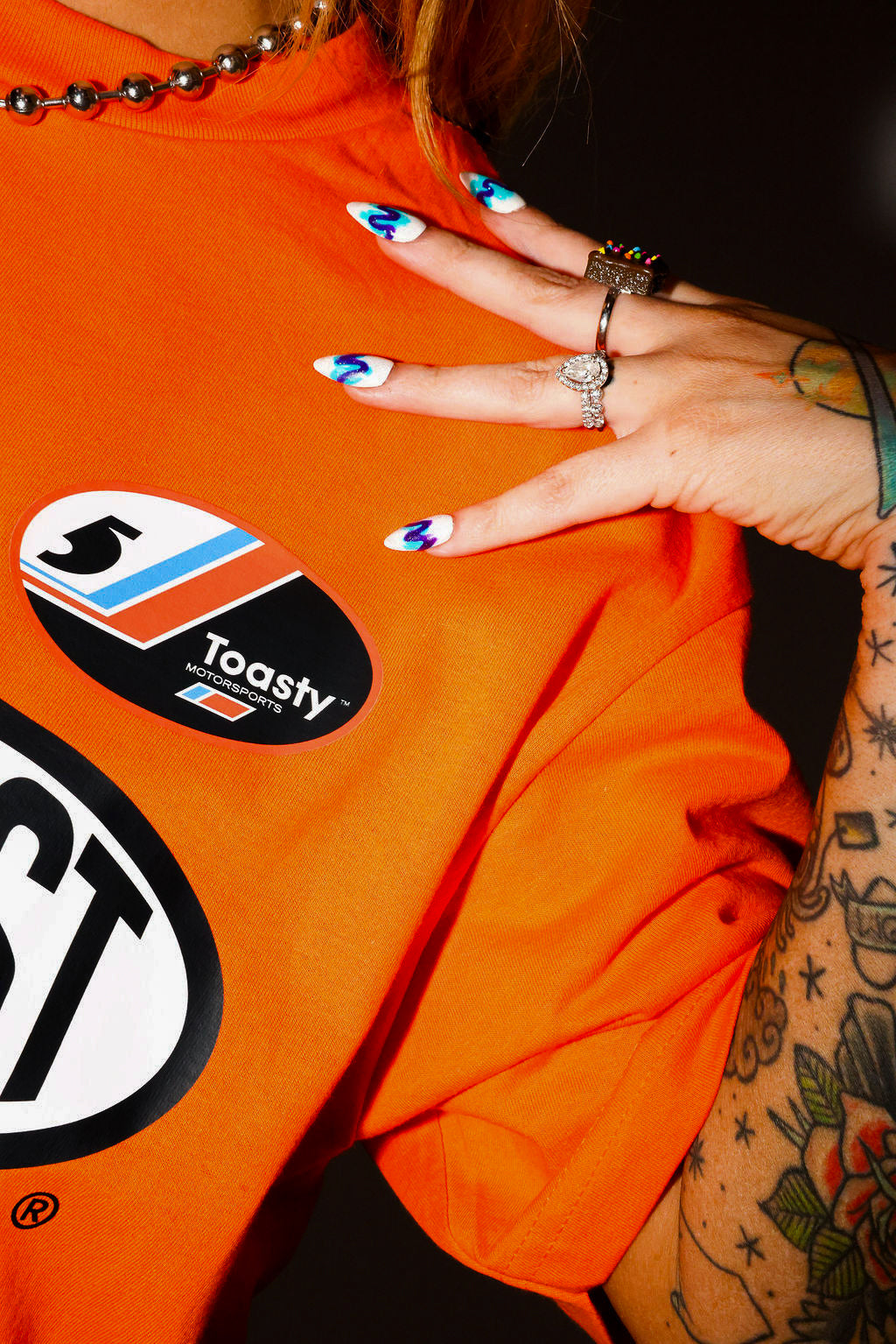 Person wearing an orange shirt with visible branding, with hand on shoulder, close up frontal view