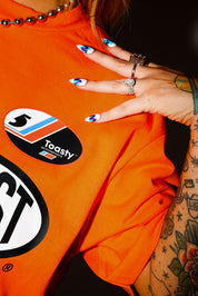 Person wearing an orange shirt with visible branding, with hand on shoulder, close up frontal view