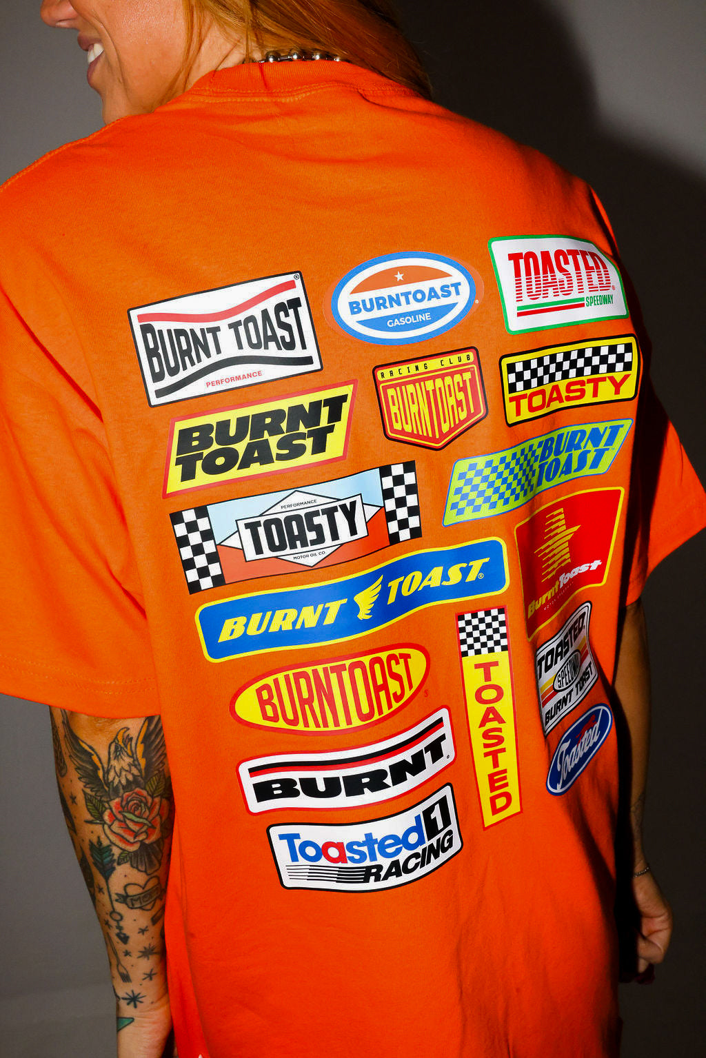 Model wearing a black trucker hat and orange shirt with 'Burntoast' branding, close up back view