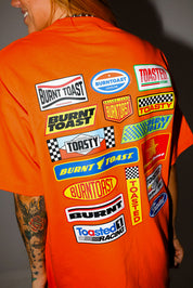 Model wearing a black trucker hat and orange shirt with 'Burntoast' branding, close up back view