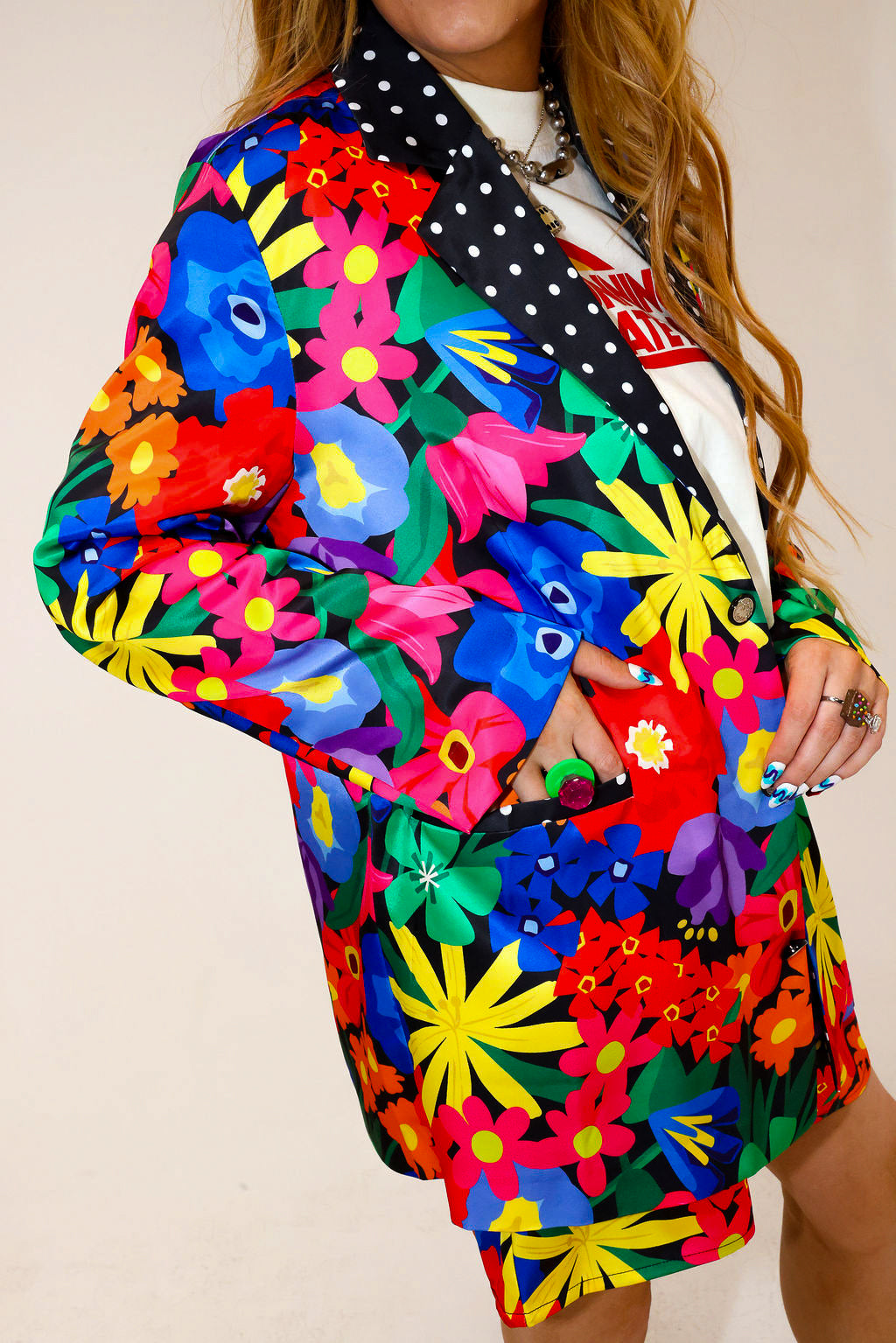 Model wearing a colorful floral jacket with polka dot collar, and matching shorts, with hand in pocket, a plain background, side view