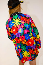 Model wearing a colorful floral jacket with polka dot collar, and matching shorts, a plain background, back view