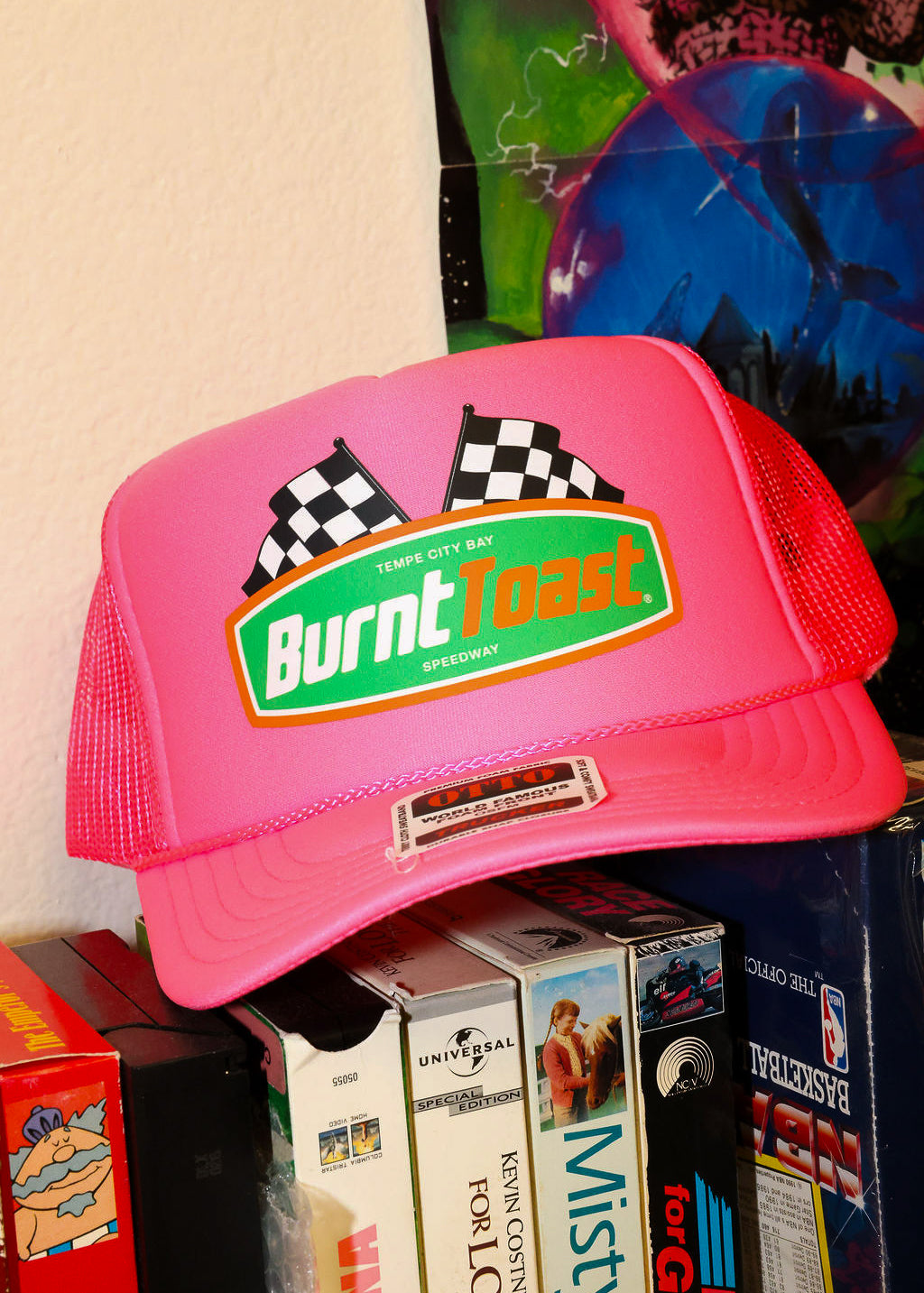 Neon pink trucker with 'Burnt Toast' logo on a stack of vintage video games, frontal view