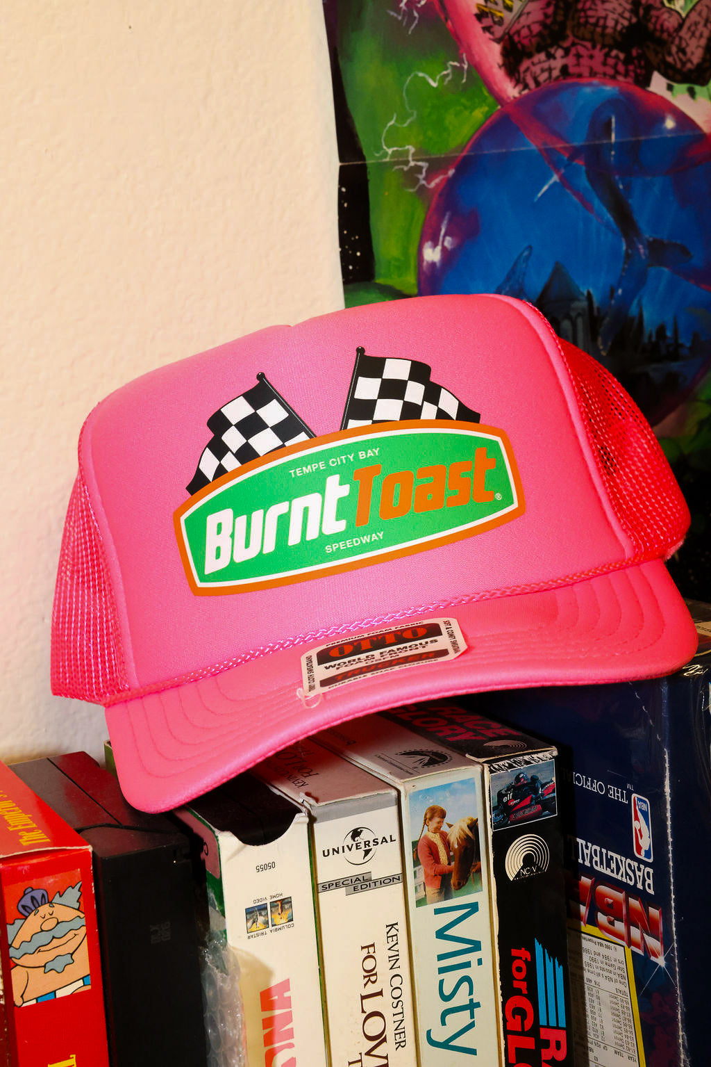 Neon pink trucker with 'Burnt Toast' logo on a stack of vintage video games, frontal view