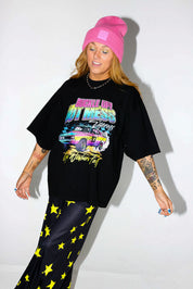 Model wearing a black short sleeve shirt with colorful graphic design and a pink beanie, and black and yellow pants, on a white background, close up frontal view