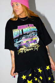 Model wearing a black short sleeve shirt with colorful graphic design and a pink beanie, and black and yellow pants, on a white background, close up frontal view