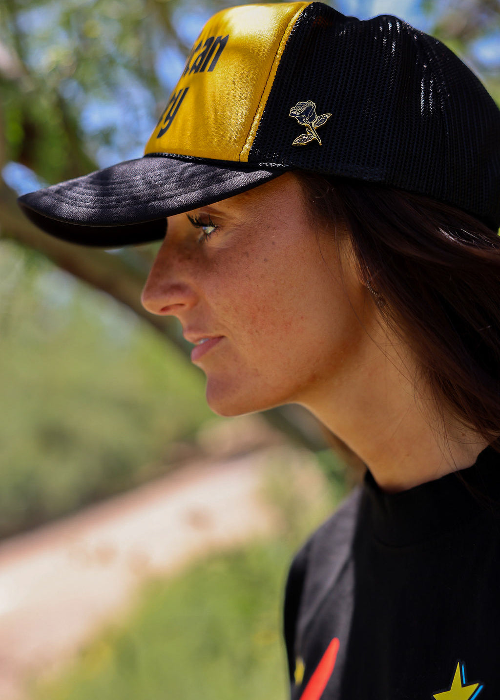 Person wearing a trucker at with 'American Honey' text and a black shirt, outdoors, close up side view