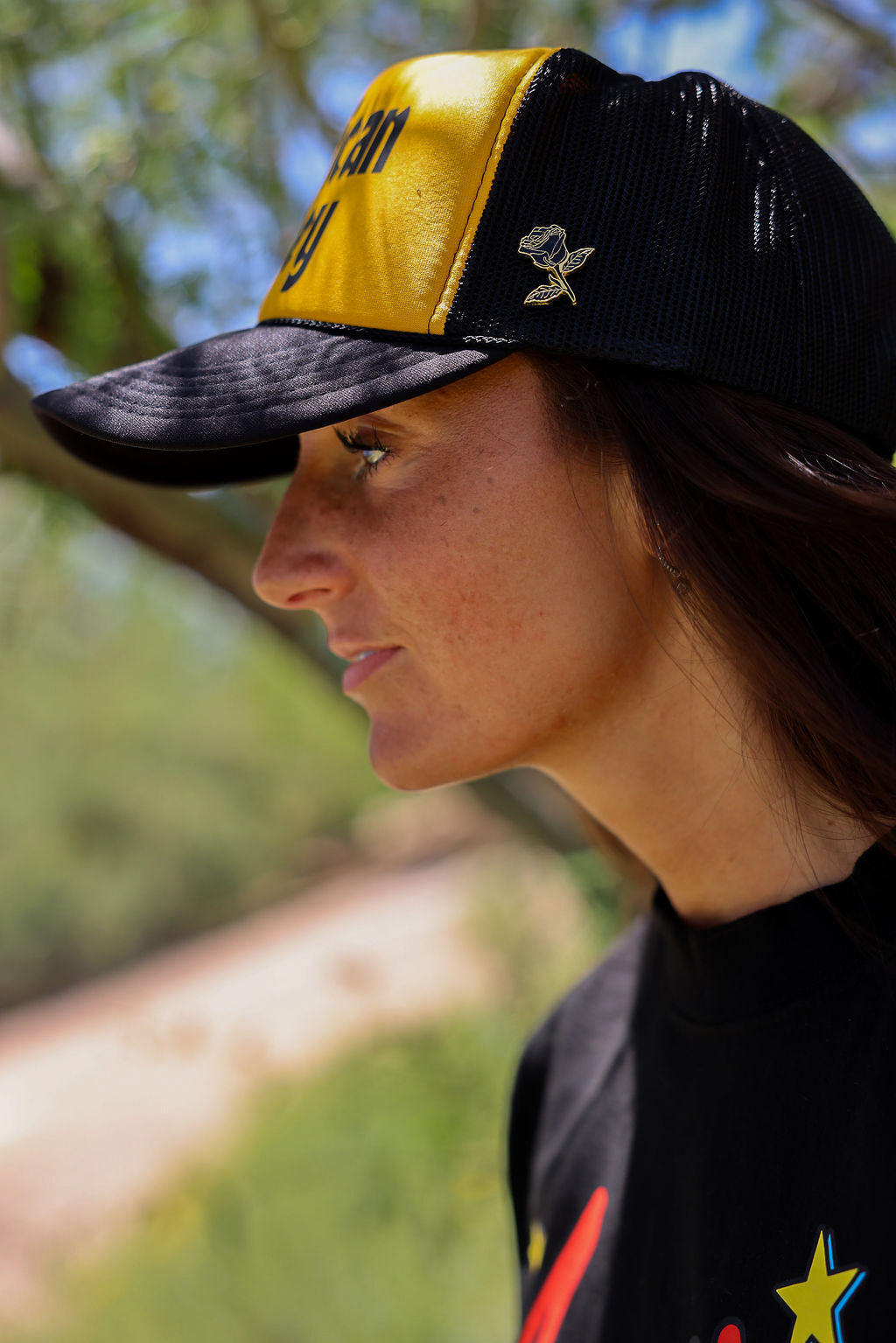 Person wearing a trucker at with 'American Honey' text and a black shirt, outdoors, close up side view