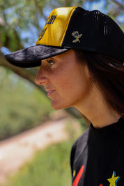 Person wearing a trucker at with 'American Honey' text and a black shirt, outdoors, close up side view