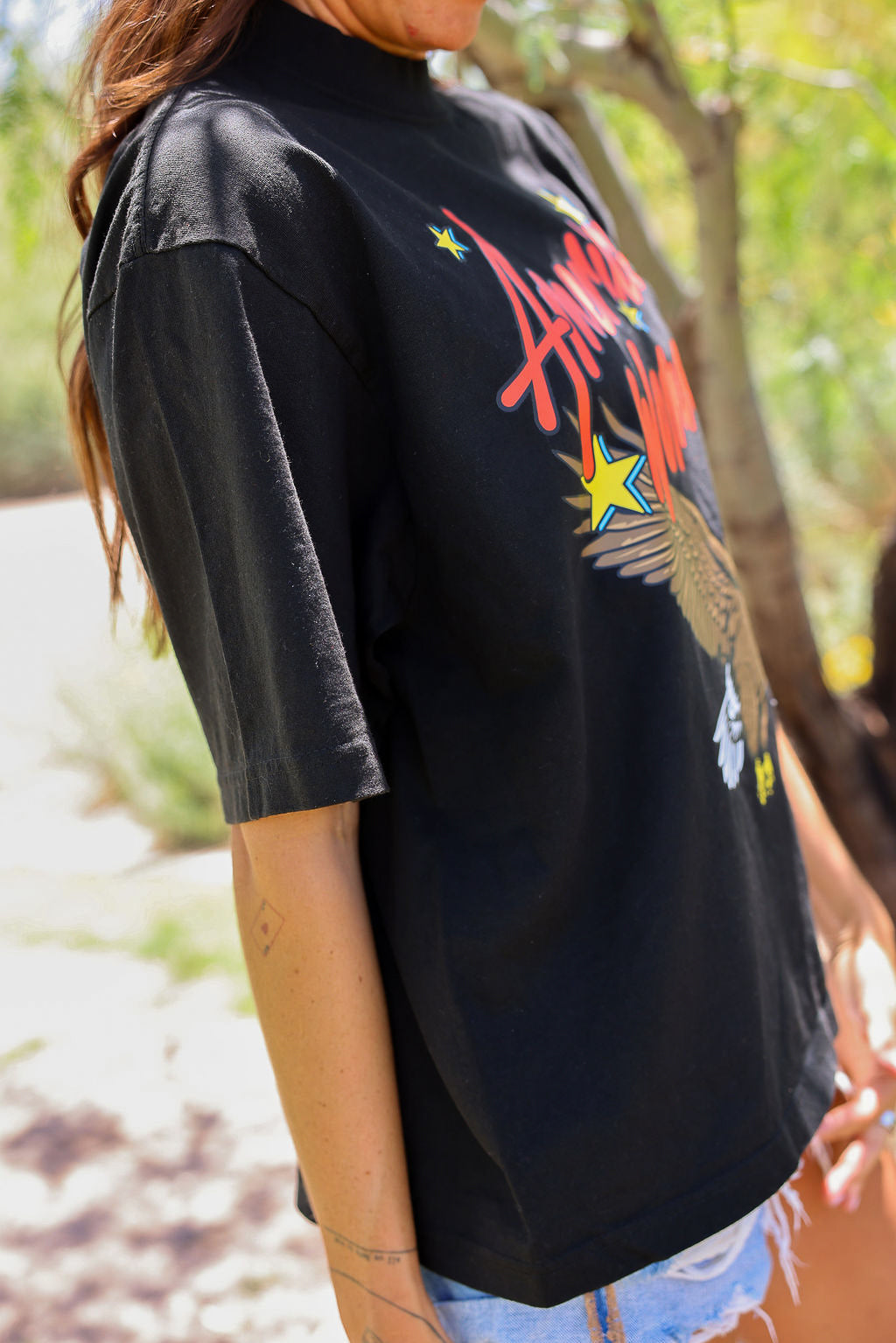 Person wearing a black t-shirt with colorful graphics outdoors, close up side view