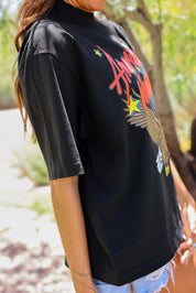 Person wearing a black t-shirt with colorful graphics outdoors, close up side view
