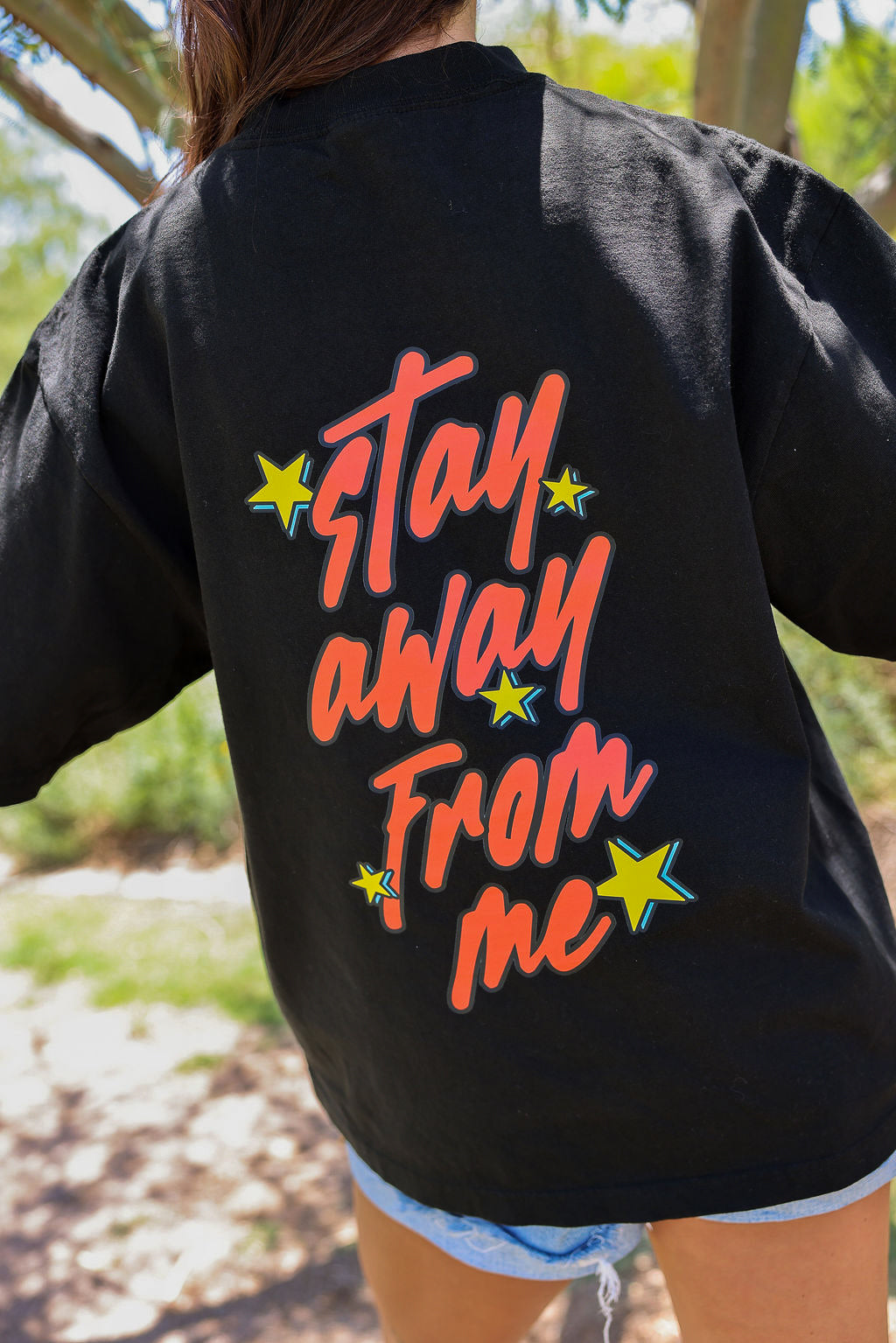 Black shirt with 'Stay Away From Me' text on the back, worn outdoors, back view