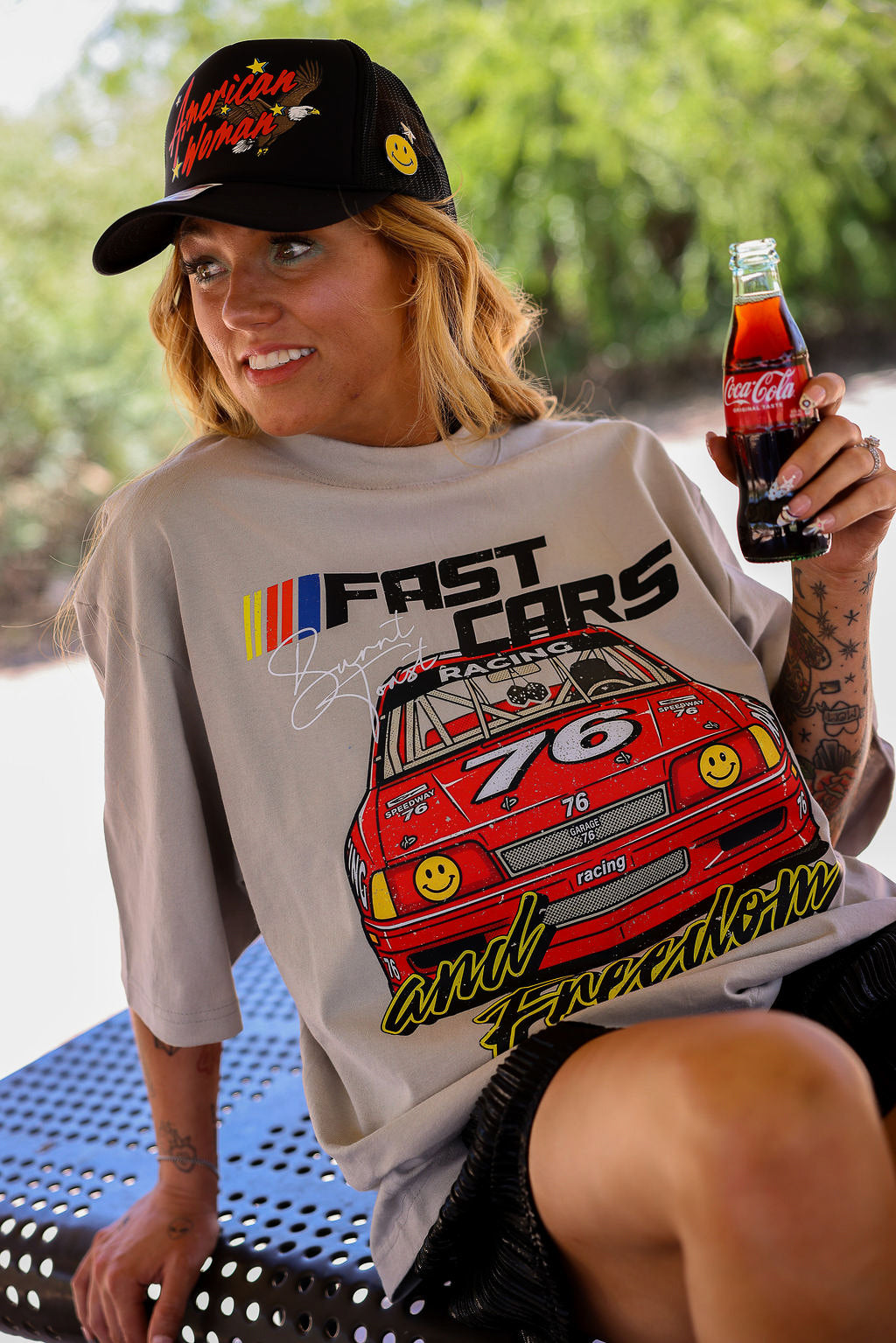 Model wearing a black trucker hat with a grey short sleeve tee with FAST CARS text and a red racing truck, sitting on a bench