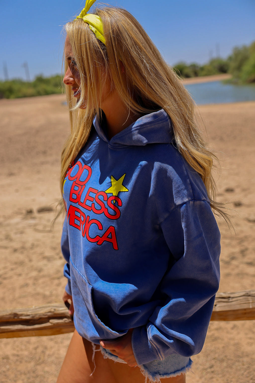 Model wearing a blue hoodie with text and graphics outdoors, side view