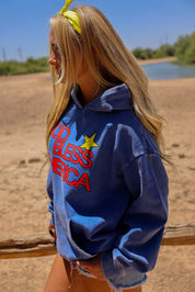 Model wearing a blue hoodie with text and graphics outdoors, side view