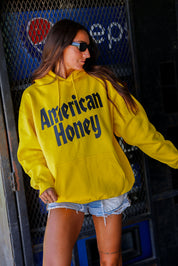 Person wearing a yellow hoodie with 'American Honey' text, standing in front of a Pepsi sign, frontal view