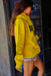 Person wearing a yellow hoodie with 'American Honey' text, standing in front of a Pepsi sign, side view