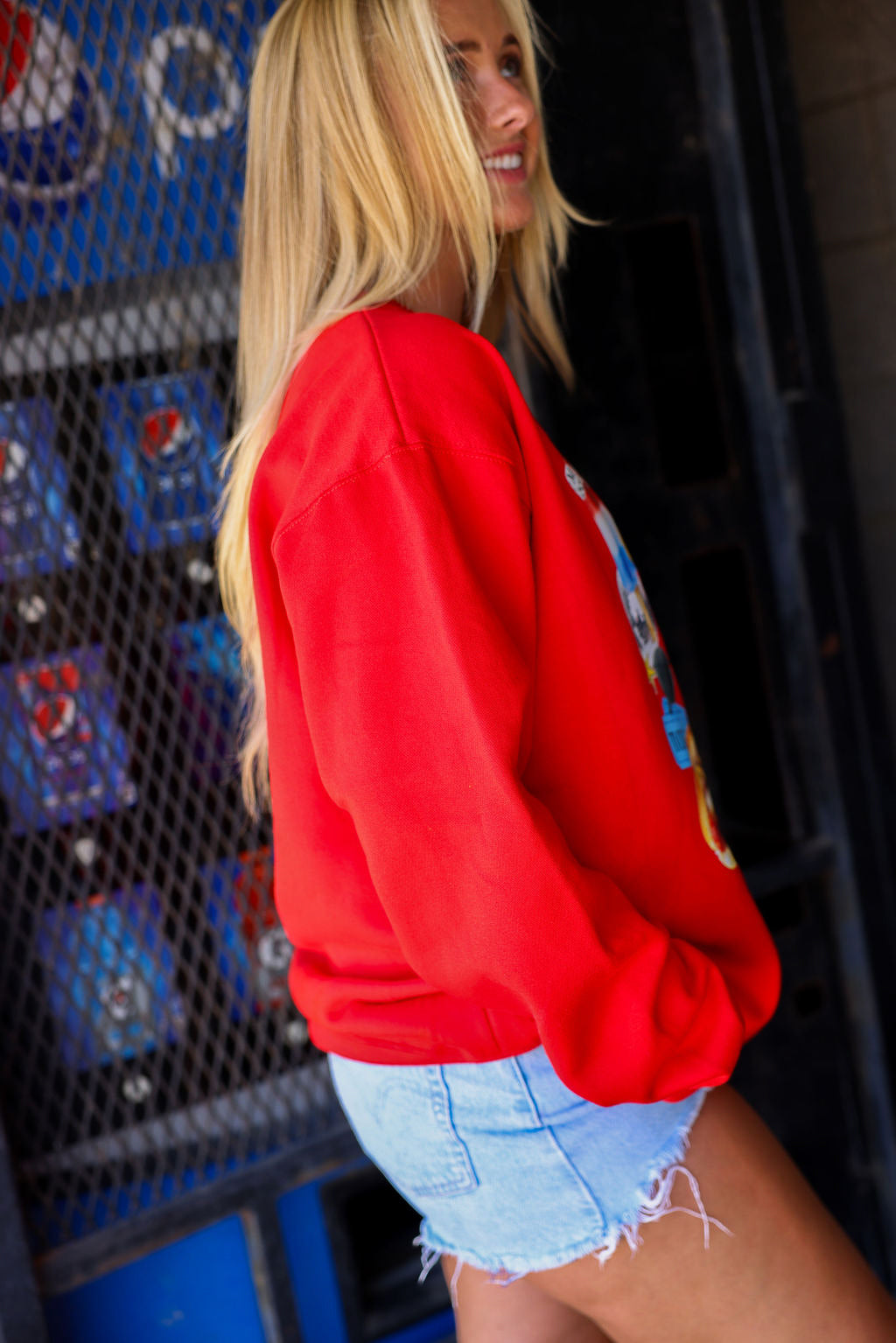 Person wearing a red sweatshirt with colorful designs in front of a Pepsi machine, side view