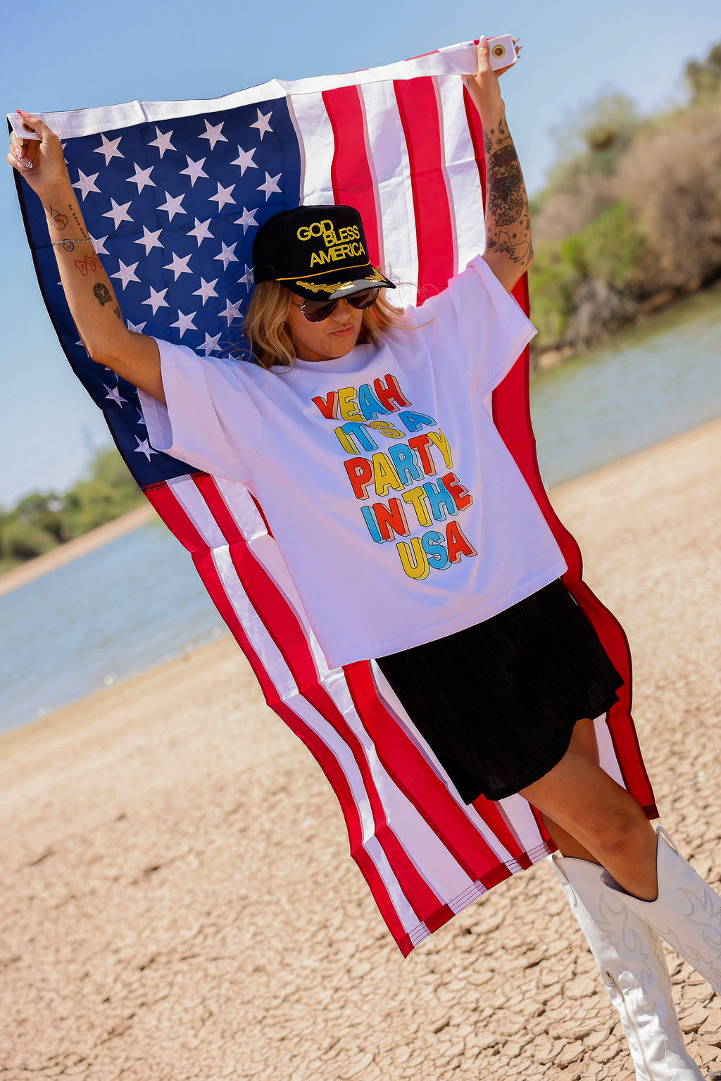 Person holding an American flag with a white shirt with colorful text, a scenic background, side view