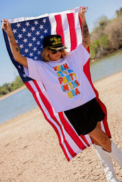 Person holding an American flag with a white shirt with colorful text, a scenic background, side view
