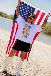 Person holding an American flag with a colorful text shirt by a body of water, frontal view