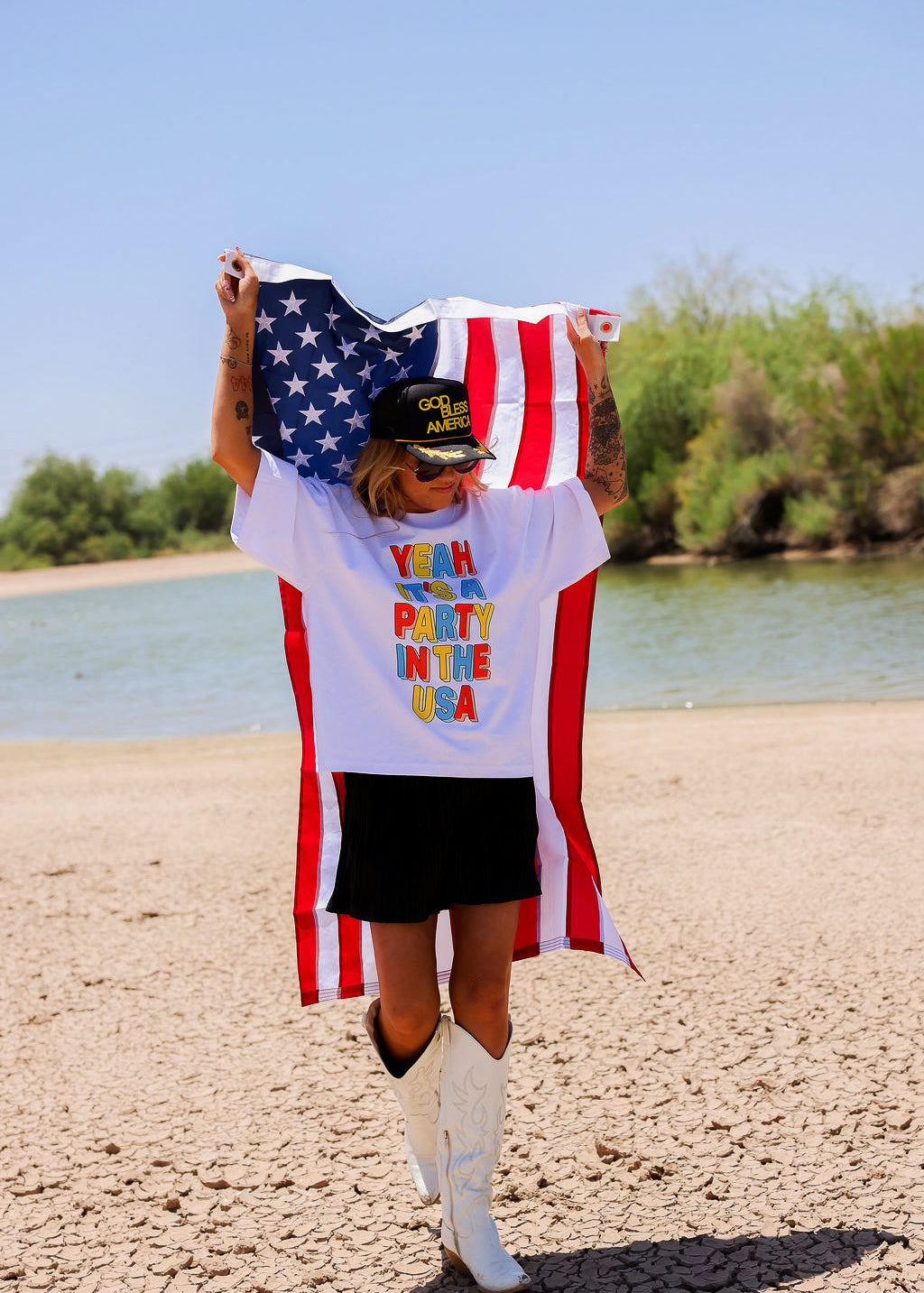 Person holding an American flag with a white shirt with colorful text, a scenic background, frontal view
