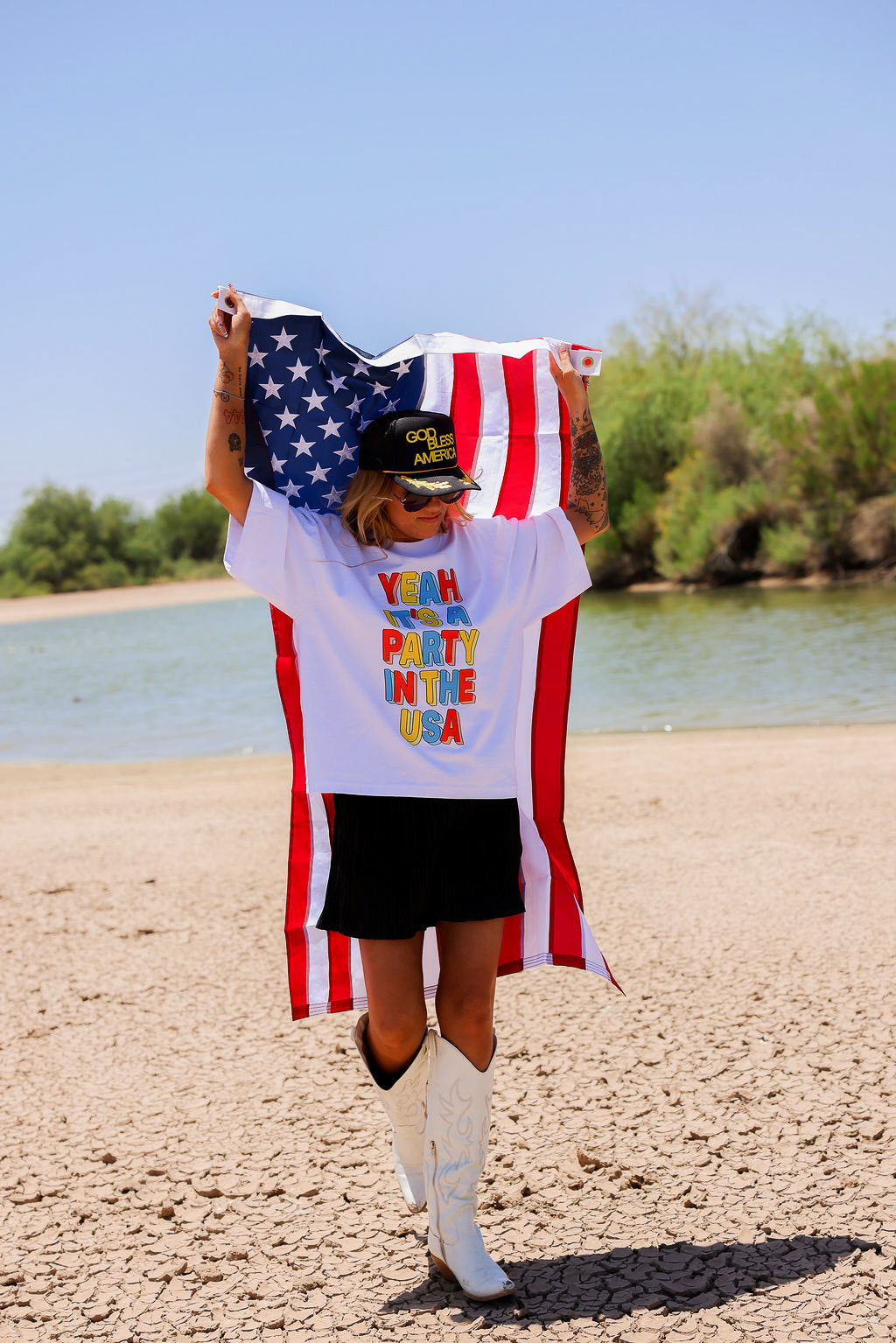 Person holding an American flag with a white shirt with colorful text, a scenic background, frontal view