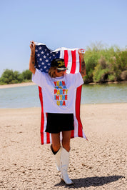 Person holding an American flag with a white shirt with colorful text, a scenic background, frontal view