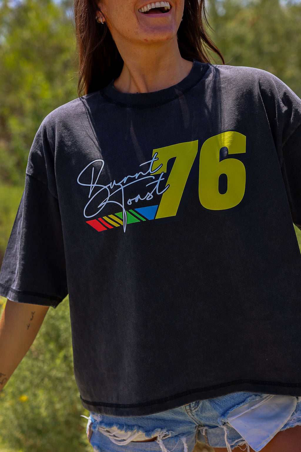 Person wearing a black t-shirt with colorful graphics and the number 76 outdoors, close up side view