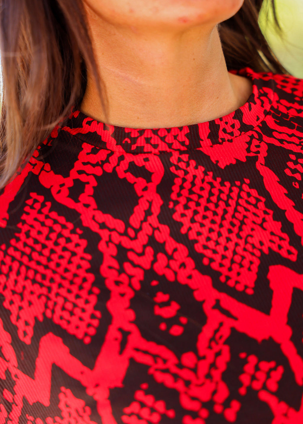 Close-up of neckline of a red and black patterned top worn by a person, frontal view