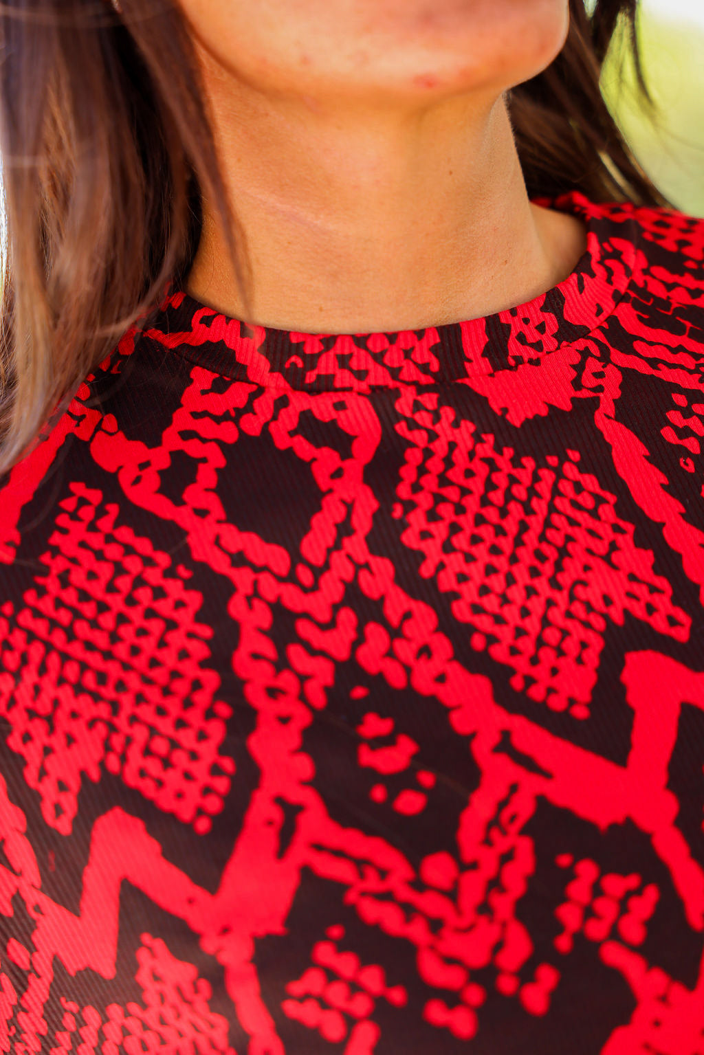 Close-up of neckline of a red and black patterned top worn by a person, frontal view