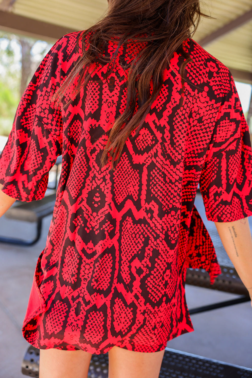 Person wearing a red and black snake skin patterned biker set with blurred background, back view