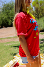 Person wearing a red t-shirt with colorful graphics outdoors, side view