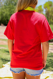 Model wearing a red short sleeve shirt outdoors, close up back view