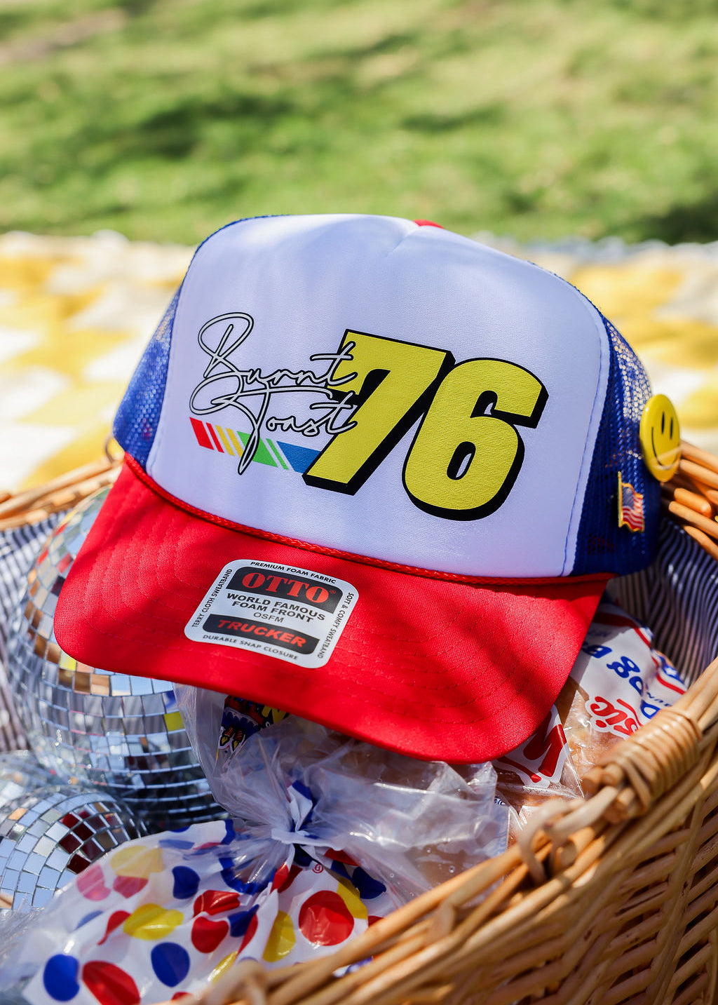 Baseball cap with number 76 and colorful design in a basket with disco ball and snacks, flat lay frontal view