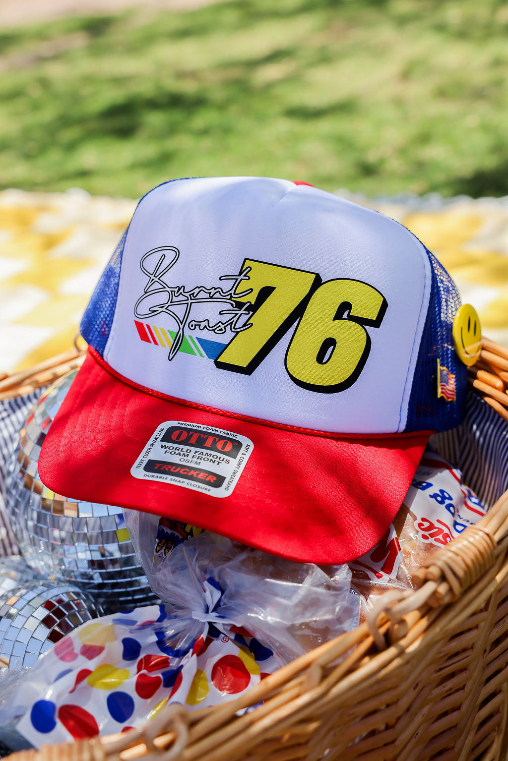 Baseball cap with number 76 and colorful design in a basket with disco ball and snacks, flat lay frontal view